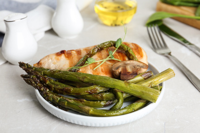 Photo of Tasty grilled chicken fillet served with asparagus on light grey marble table