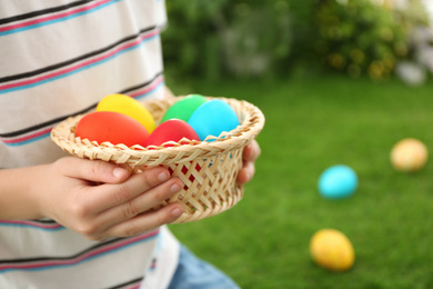 Cute little boy with basket full of Easter eggs outdoors, closeup