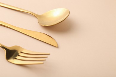 Stylish golden cutlery set on beige background, closeup. Space for text