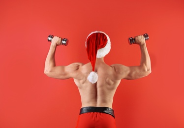 Young muscular man in Santa hat with dumbbells on color background
