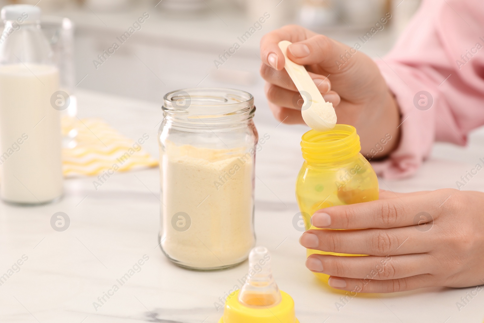 Photo of Woman preparing infant formula at table indoors, closeup. Baby milk