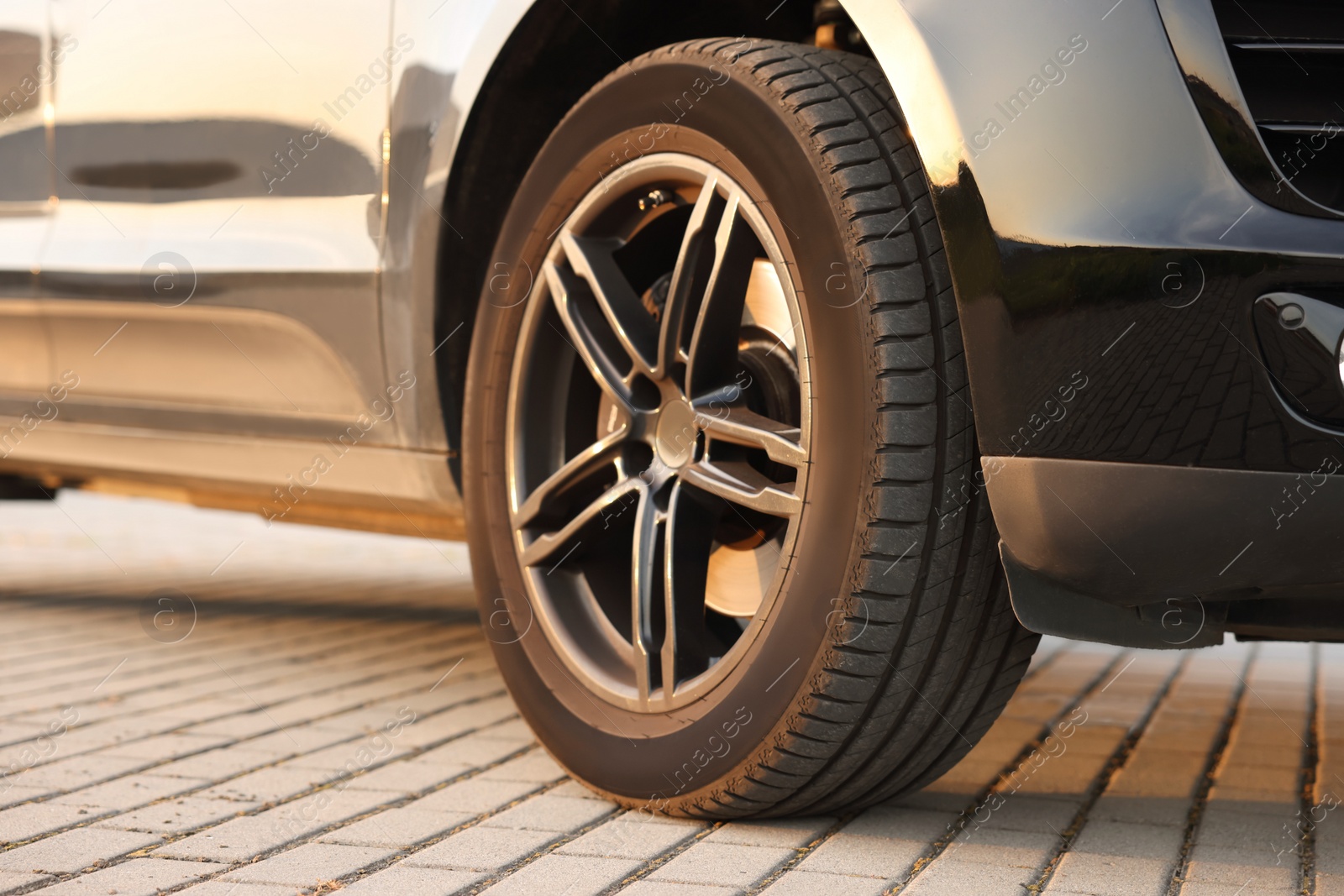 Photo of Modern car with big wheel parked on stone pavement outdoors, closeup