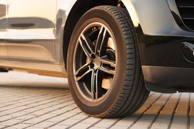 Modern car with big wheel parked on stone pavement outdoors, closeup