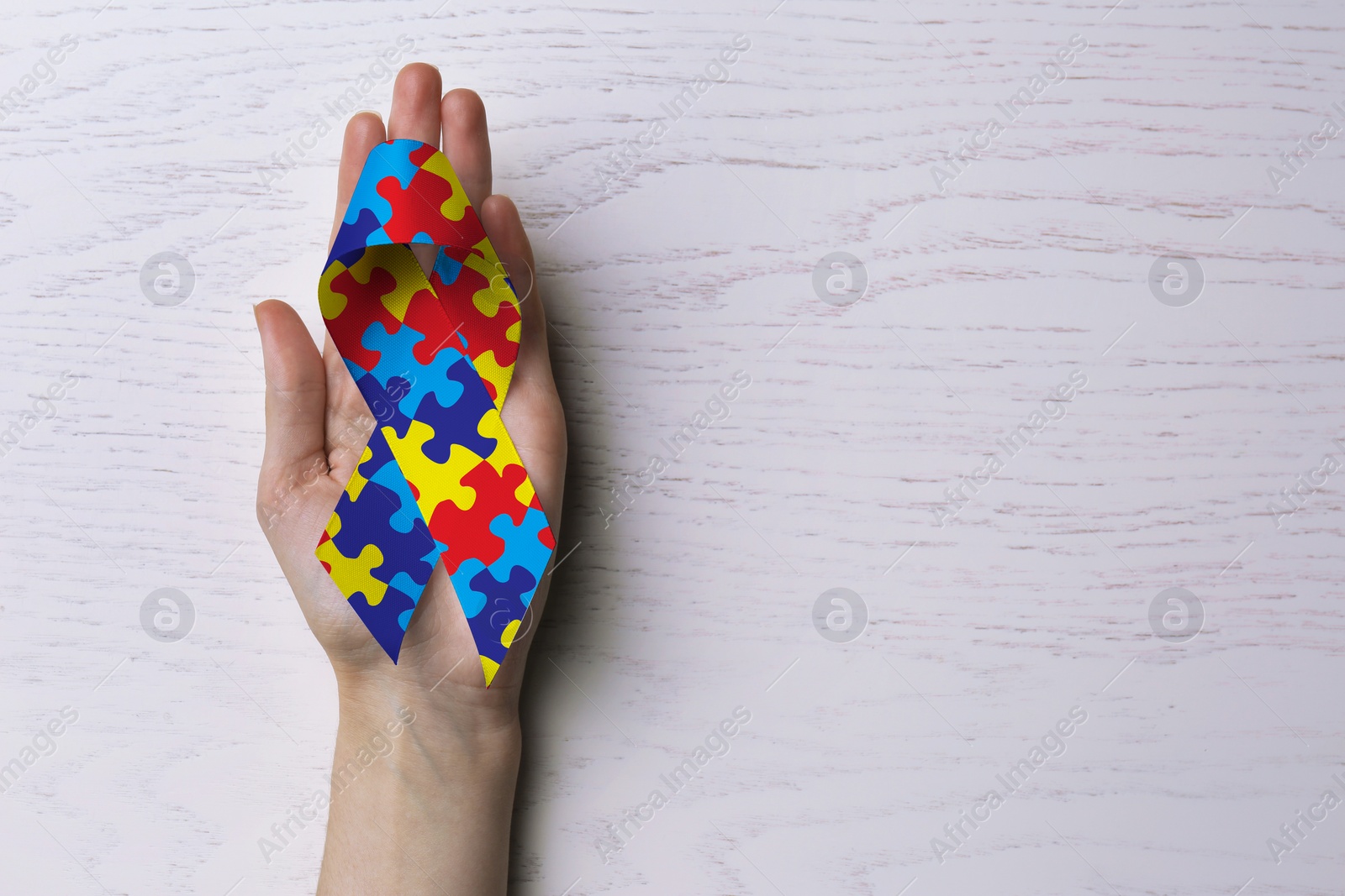 Image of World Autism Awareness Day. Woman with colorful puzzle ribbon on white wooden background, top view with space for text