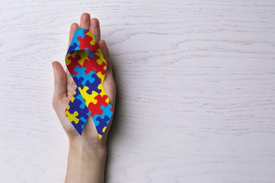 Image of World Autism Awareness Day. Woman with colorful puzzle ribbon on white wooden background, top view with space for text