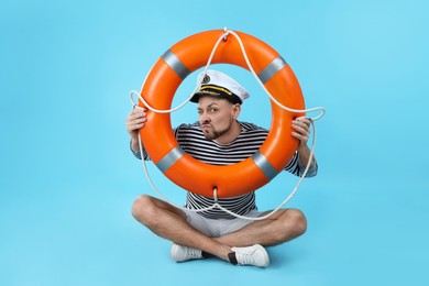 Photo of Funny sailor with orange ring buoy on light blue background