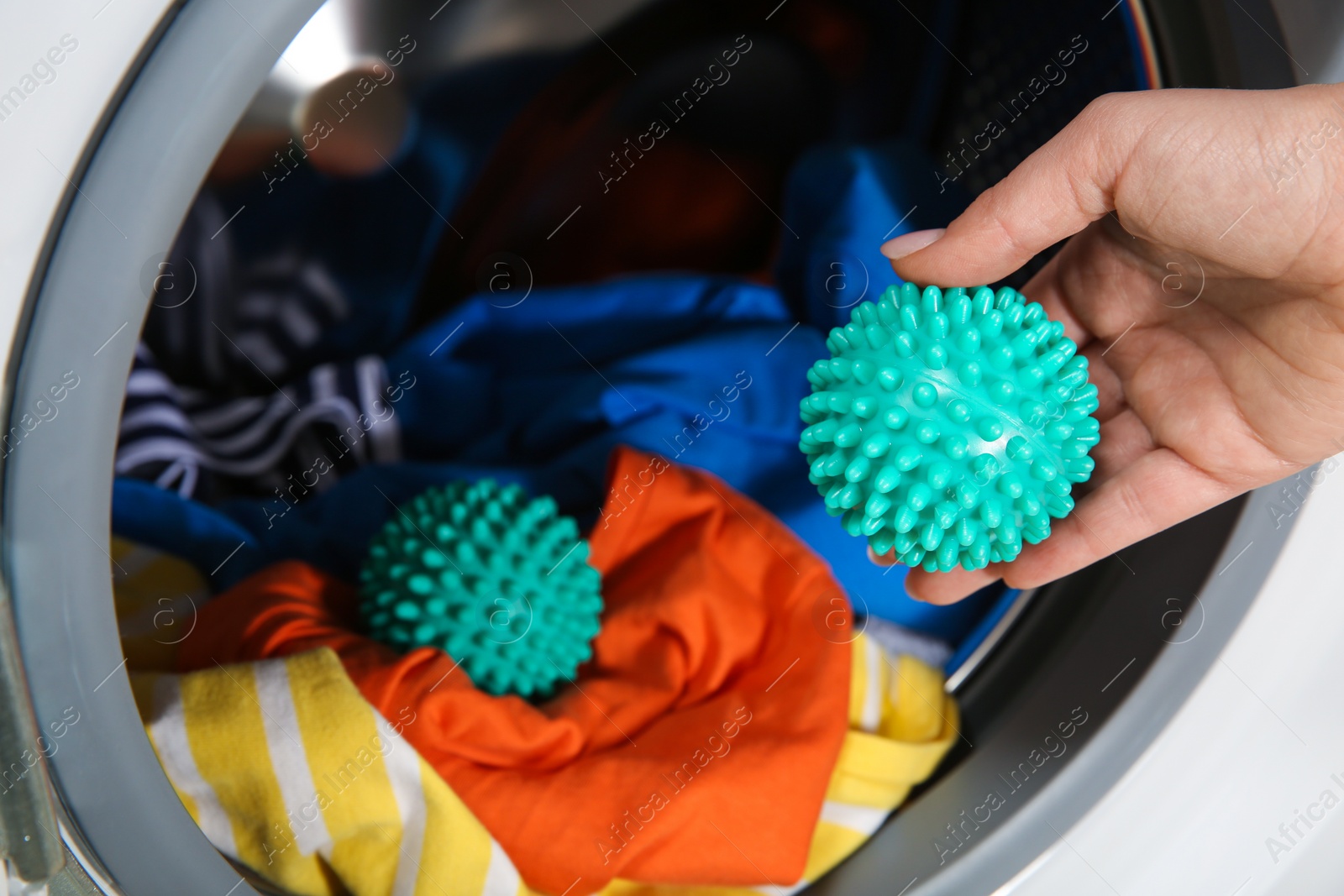 Photo of Woman putting green dryer ball into washing machine, closeup