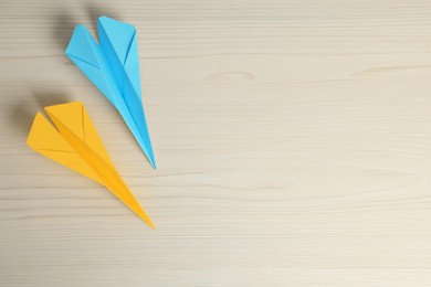 Photo of Handmade paper planes in light blue and yellow colors on beige wooden table, flat lay. Space for text