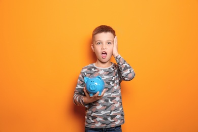 Photo of Emotional little boy with piggy bank on color background