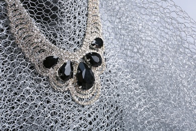 Elegant necklace on stand with silver mesh fabric, space for text. Luxury jewelry