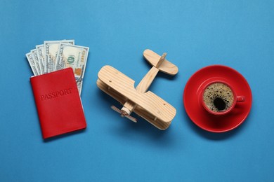 Photo of Flat lay composition with passport, wooden model of plane and dollars on blue table. Business trip