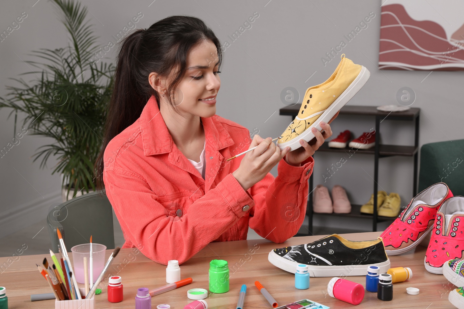 Photo of Woman painting on sneaker at wooden table indoors. Customized shoes