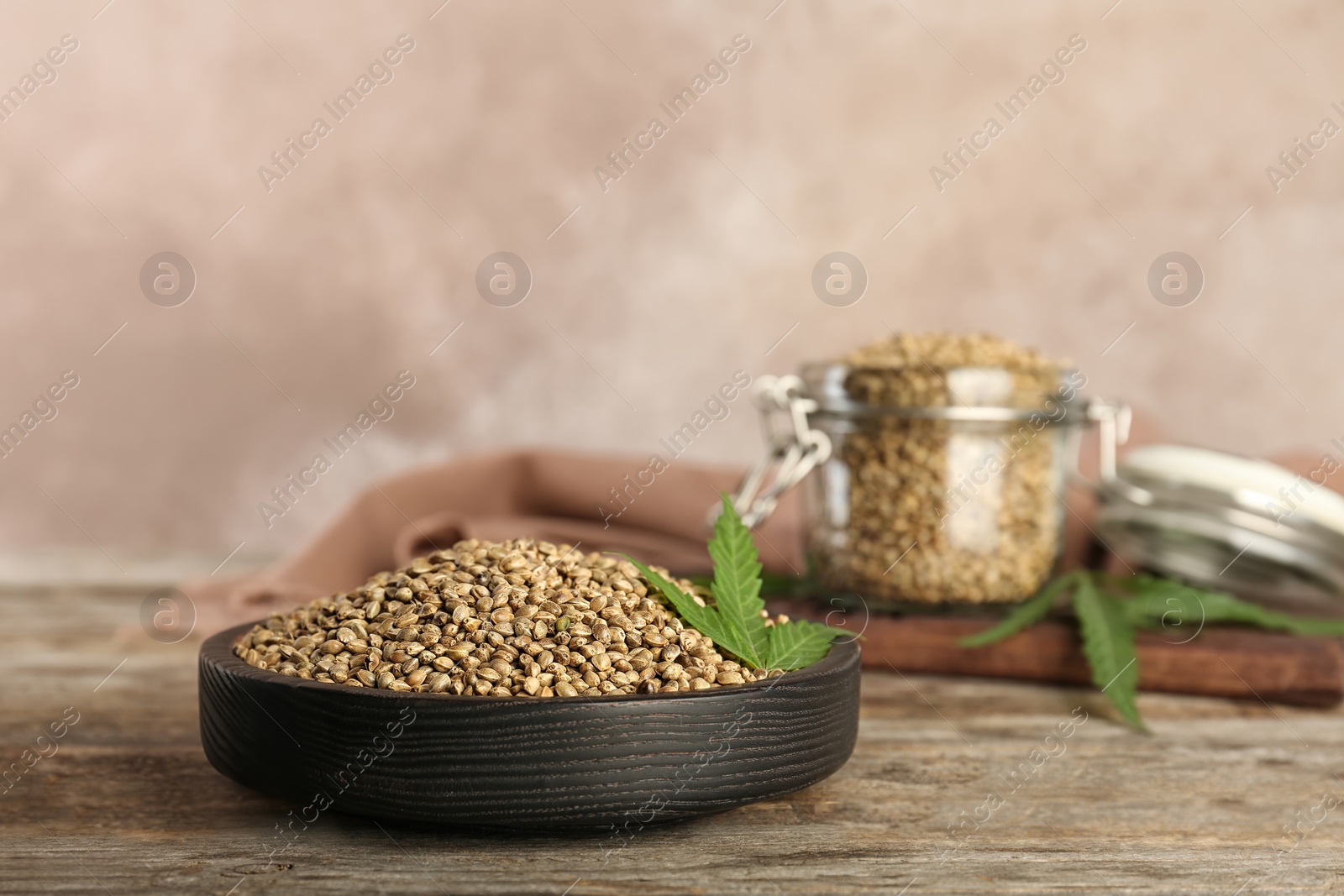 Photo of Bowl of hemp seeds on wooden table against color background