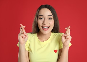 Photo of Excited young woman holding fingers crossed on red background. Superstition for good luck