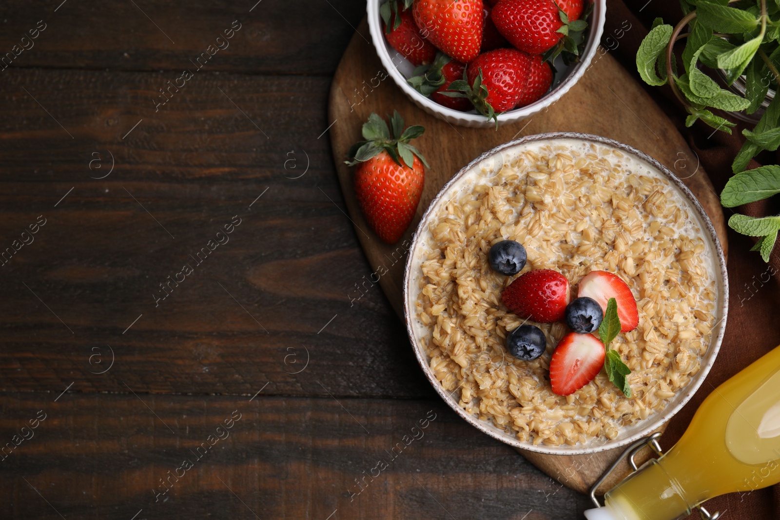 Photo of Tasty oatmeal with strawberries and blueberries in bowl on wooden table, flat lay. Space for text