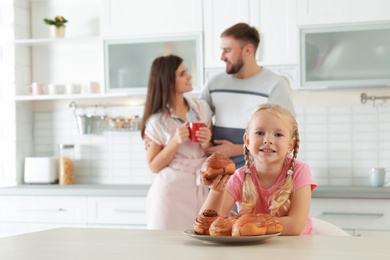 Photo of Little girl with freshly oven baked buns at table in kitchen