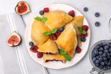 Plate of delicious samosas, berries and mint leaves on light table, flat lay