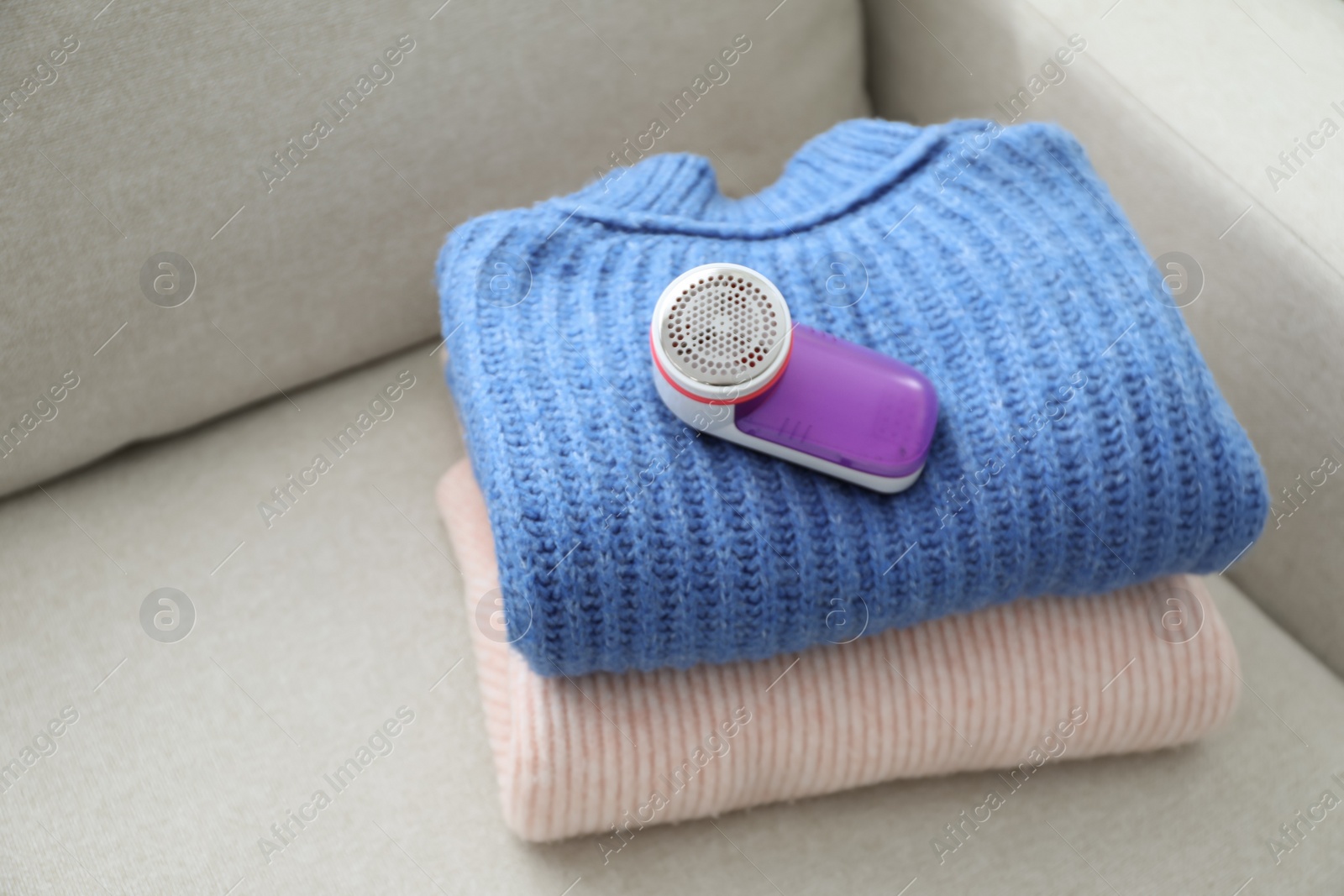 Photo of Modern fabric shaver and woolen sweaters on sofa indoors