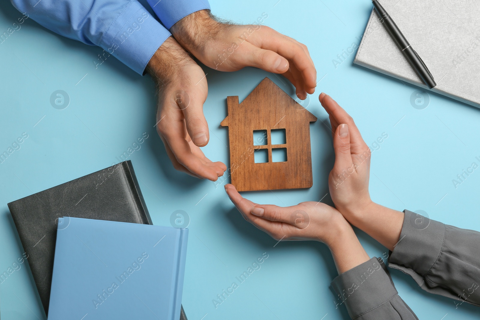 Photo of Couple holding hands near figure of house on color background, top view. Home insurance