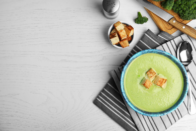 Photo of Delicious broccoli cream soup with croutons served on wooden table, flat lay. Space for text