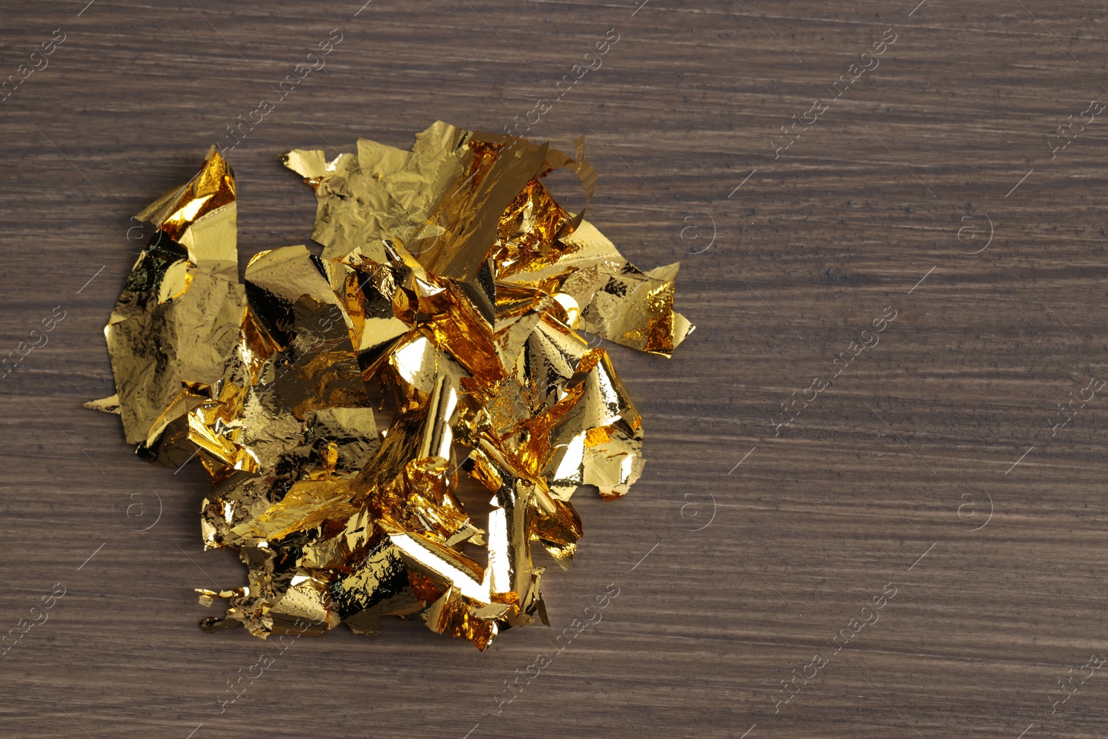 Photo of Pieces of edible gold leaf on wooden table, top view. Space for text