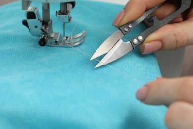 Photo of Seamstress with tailor's scissors working with sewing machine, closeup