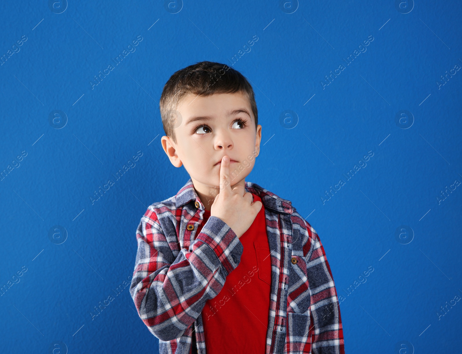 Photo of Thoughtful little boy in casual outfit on blue background