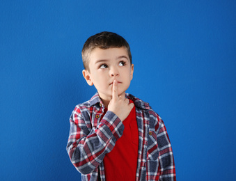 Photo of Thoughtful little boy in casual outfit on blue background
