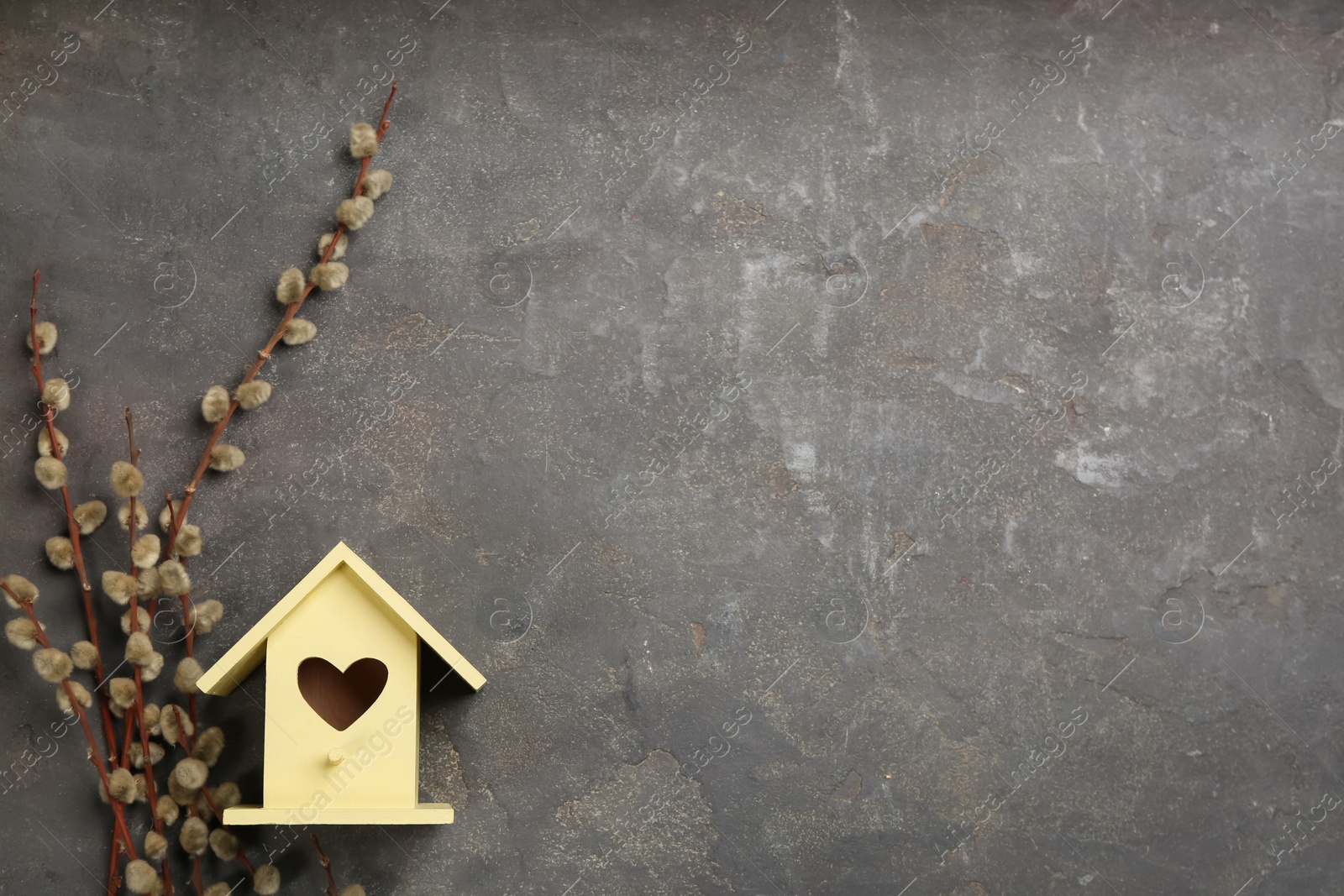 Photo of Beautiful bird house with heart shaped hole and willow branches on grey background, space for text. Spring flat lay composition