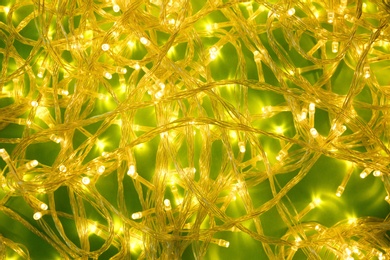 Glowing Christmas lights on green background, top view