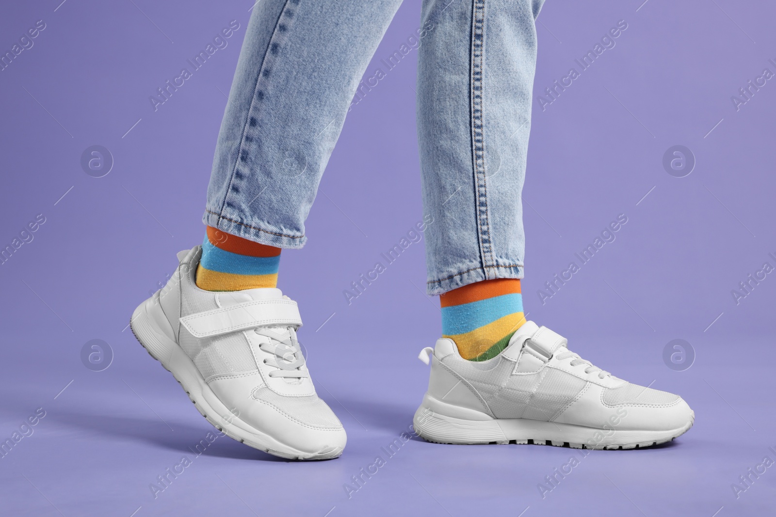 Photo of Woman in stylish colorful socks, sneakers and jeans on violet background, closeup