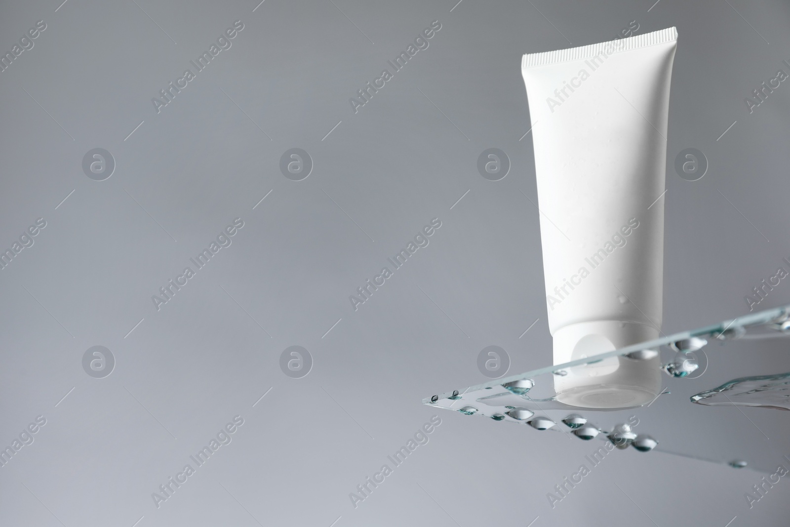 Photo of Tube with moisturizing cream on glass against grey background, low angle view. Space for text