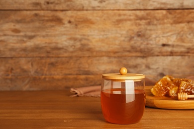 Photo of Glass jar with sweet honey on table against wooden background. Space for text