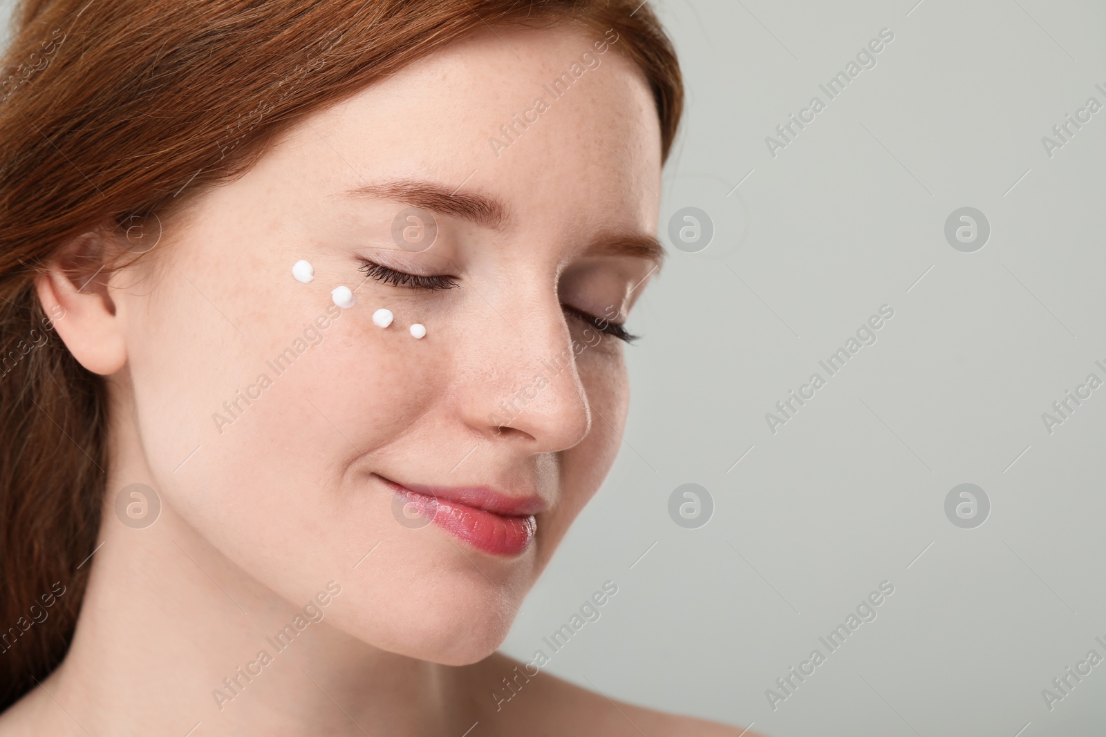 Photo of Beautiful woman with freckles and cream on her face against grey background, closeup. Space for text