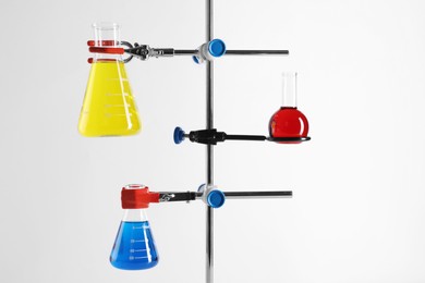 Retort stand and laboratory flasks with liquids on white background