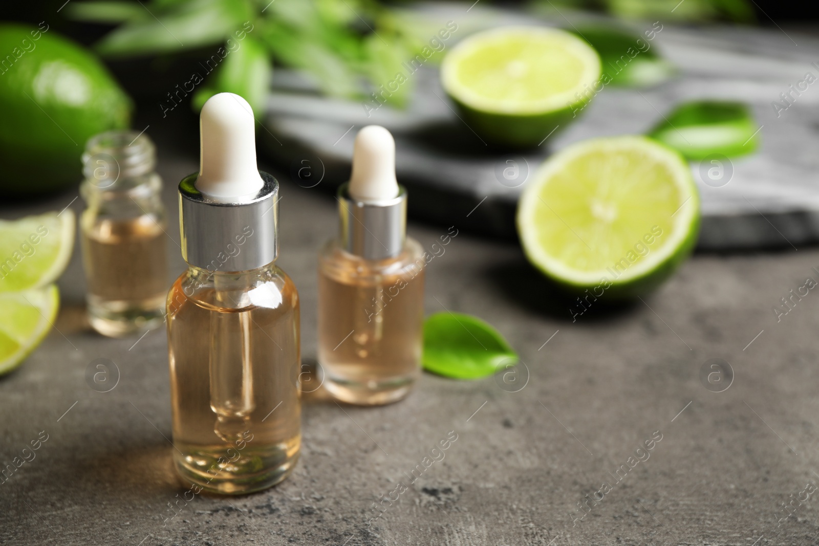 Photo of Lime essential oil and cut citrus fruits on grey table. Space for text