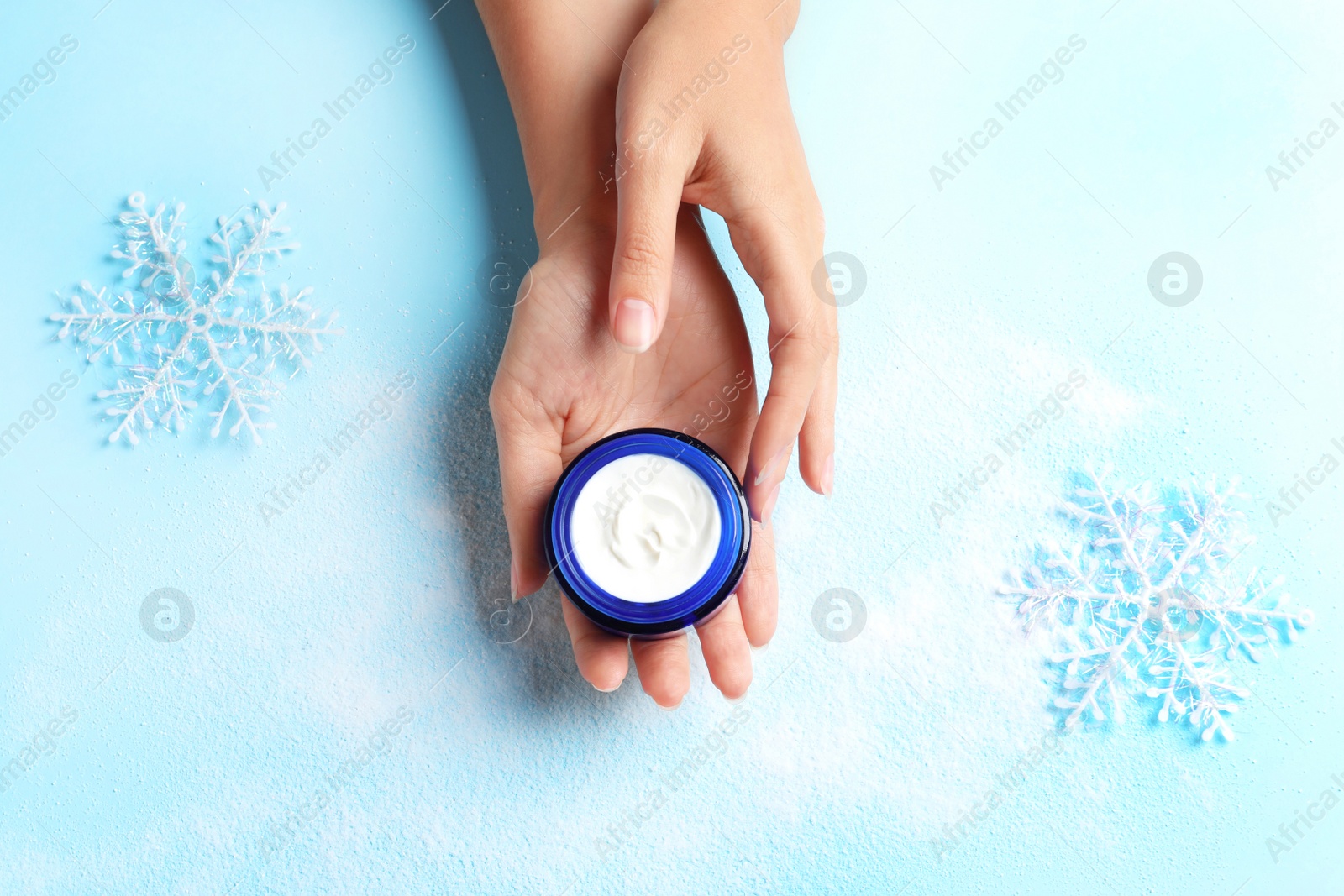 Photo of Woman holding jar of moisturizing cream on color background, top view. Winter skin care cosmetic