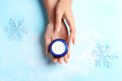 Woman holding jar of moisturizing cream on color background, top view. Winter skin care cosmetic