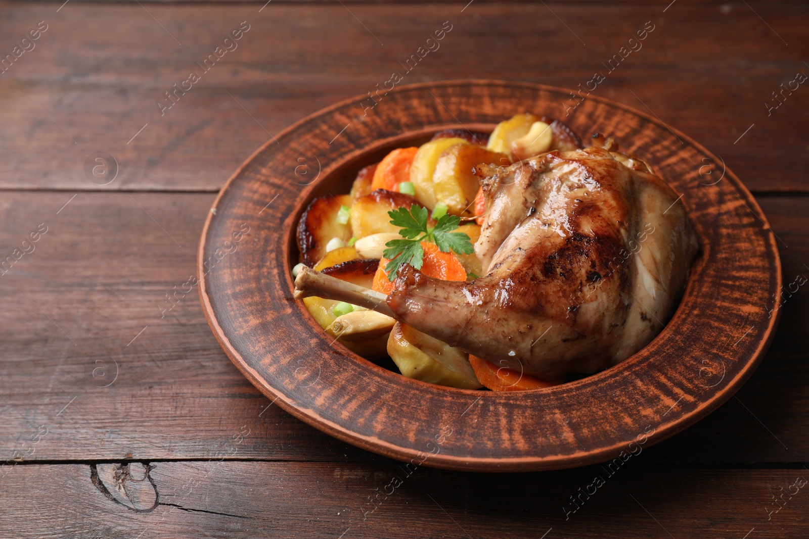 Photo of Tasty cooked rabbit meat with vegetables on wooden table. Space for text