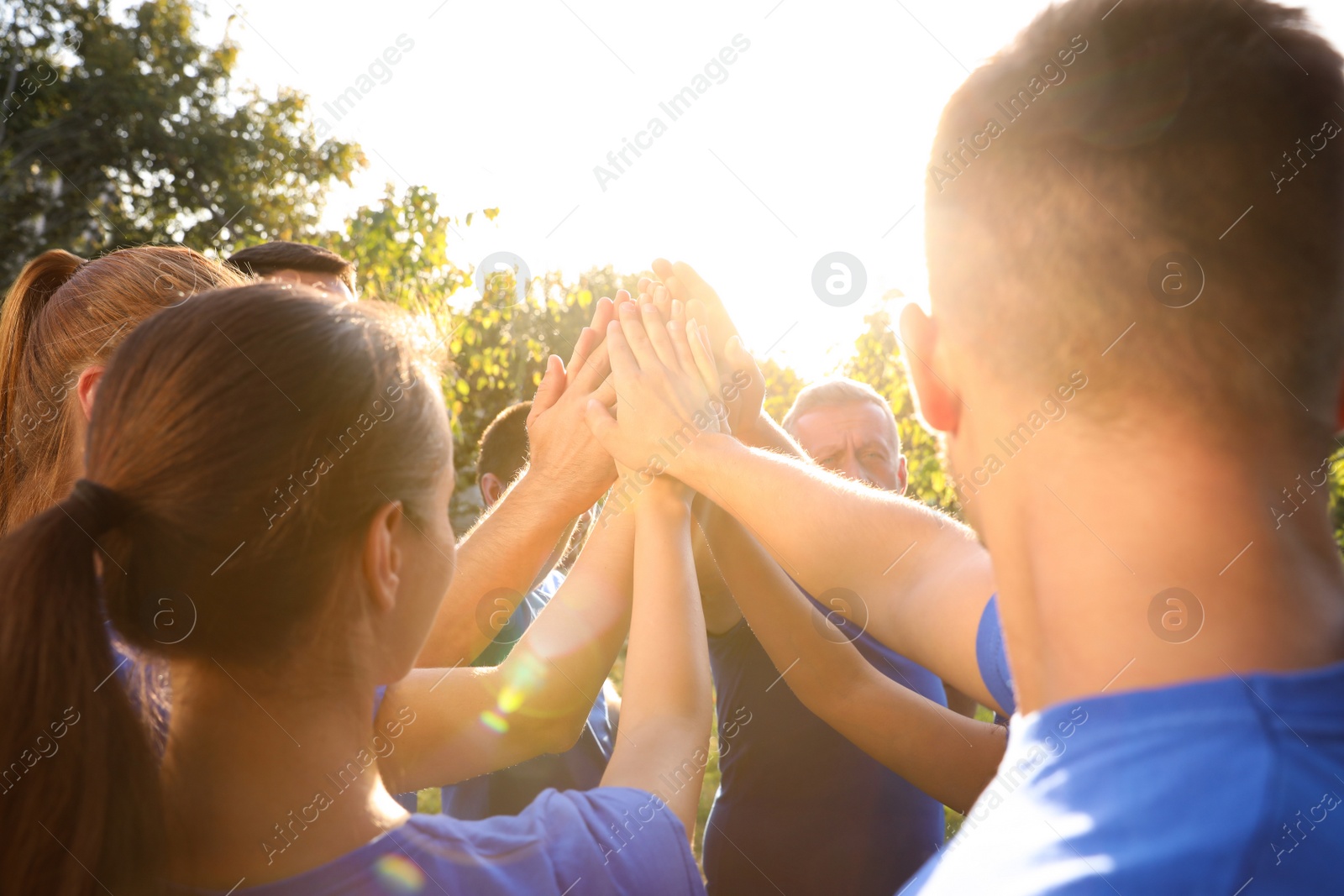 Photo of Group of volunteers joining hands together outdoors on sunny day