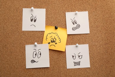 Photo of Yellow paper note with drawn sad face among aggressive ones pinned to cork board. Racism concept