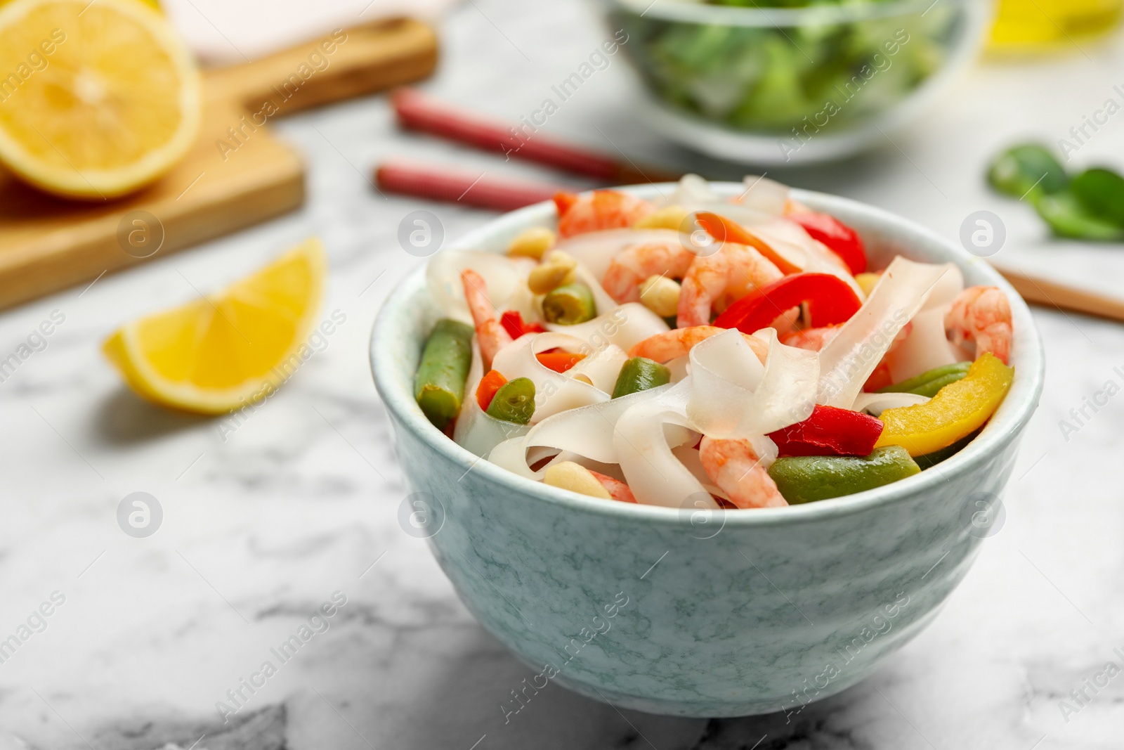 Photo of Tasty cooked rice noodles with shrimps and vegetables on white marble table