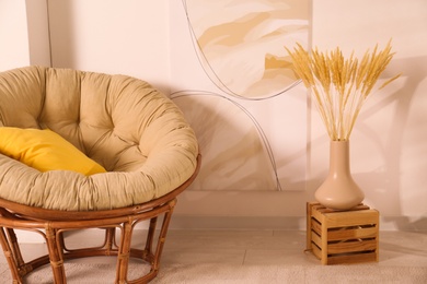 Vase with decorative dried plants and painting near papasan chair in stylish room interior