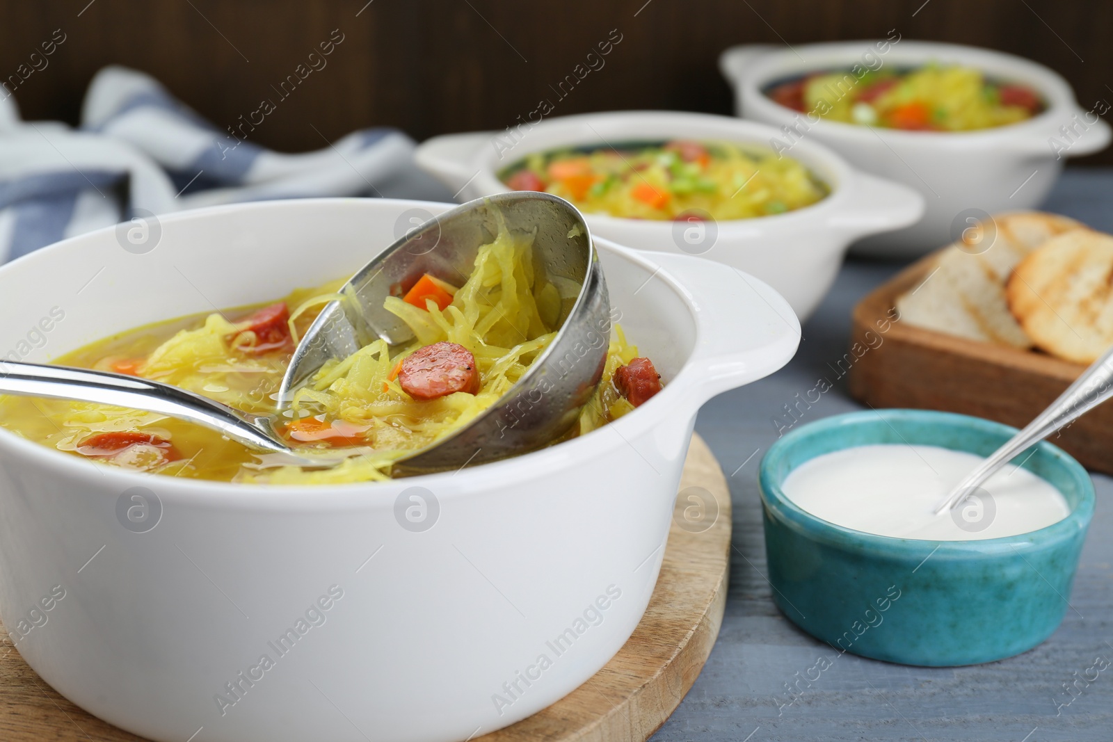 Photo of Delicious sauerkraut soup with smoked sausages and ladle on table, closeup