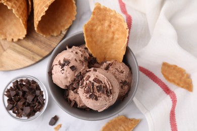 Photo of Bowl of tasty chocolate ice cream with chocolate chunks and pieces of waffle cone on white table, flat lay