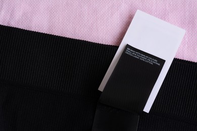 Clothing label with care information on black garment, top view. Space for text