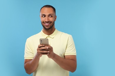 Photo of Happy man sending message via smartphone on light blue background, space for text