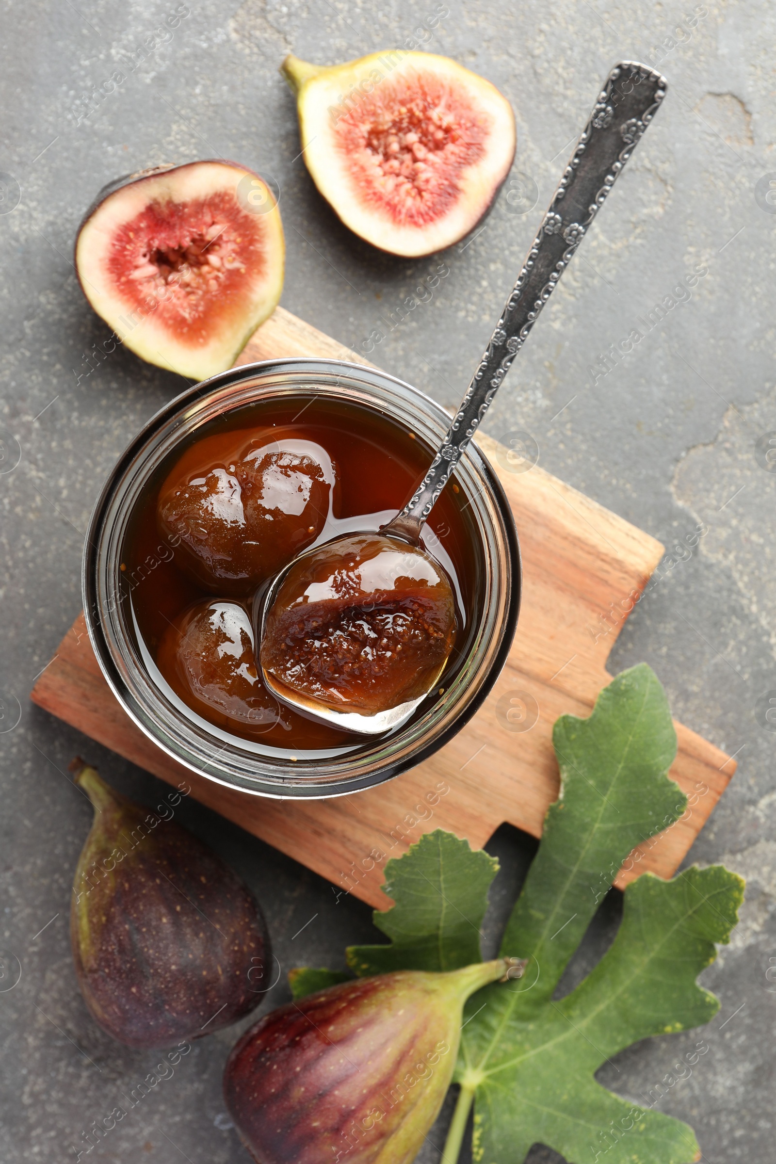 Photo of Jar of tasty sweet jam, fresh figs and green leaf on grey table, flat lay