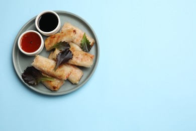 Photo of Tasty fried spring rolls, lettuce and sauces on light blue table, top view. Space for text