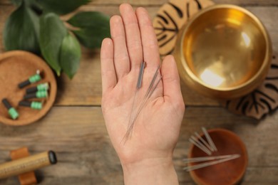 Photo of Woman holding many acupuncture needles over wooden table, top view